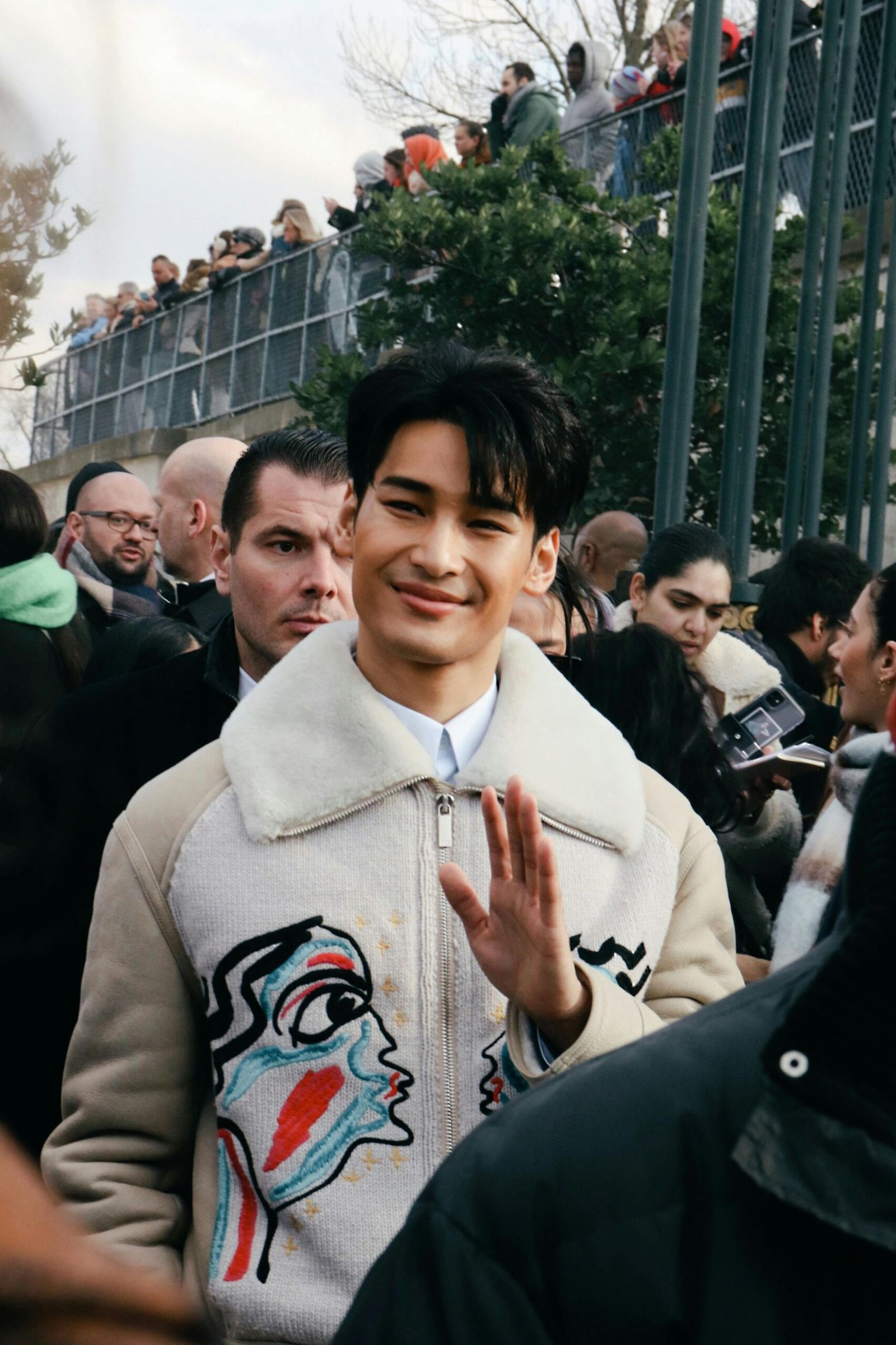 Smiling man among a crowd on a lively Paris street, capturing modern fashion and public event atmosphere.